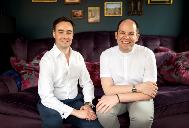 Hugh and Ben, owners of Huben Travel, on a sofa in their home