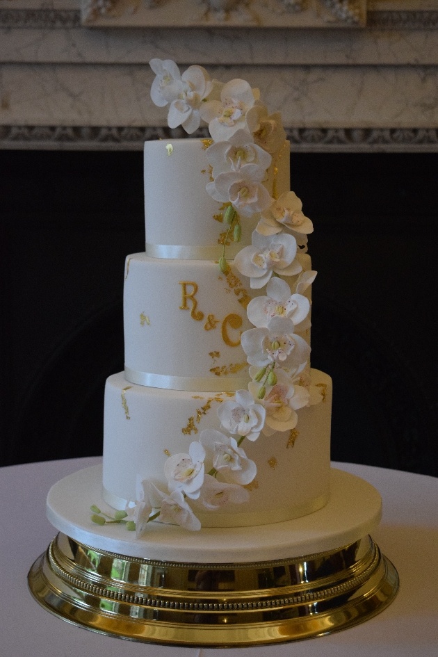 White wedding cake with couple's initials in gold and orchid sugar flowers