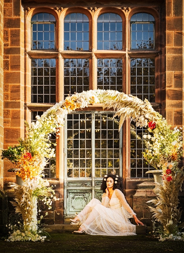 bride sitting on steps at thornton manor beneath a floral arch