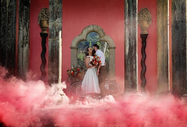 bride and groom kiss surrounded by a red smoke bomb in portmerion
