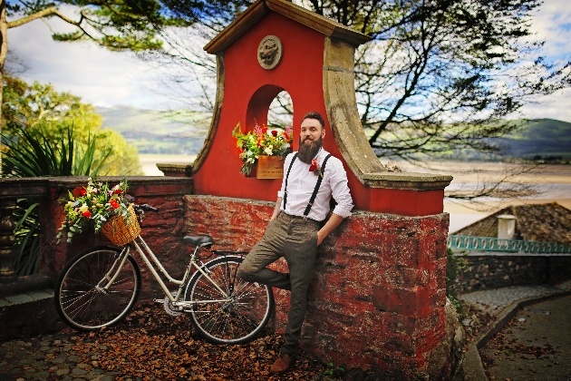 groom leans against a wall with the north wales coast in the background