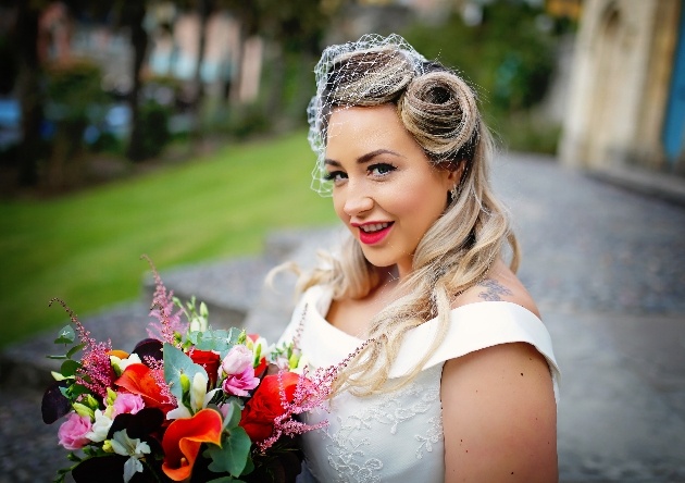 bride with vintage retro style hair and fascinator holding bouquet