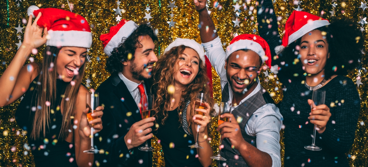 Five people celebrating at a christmas party with champagne and wearing Santa hats