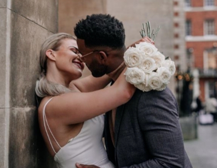 couple kissing up the side of a building in wedding outfits bride holding bouquet 