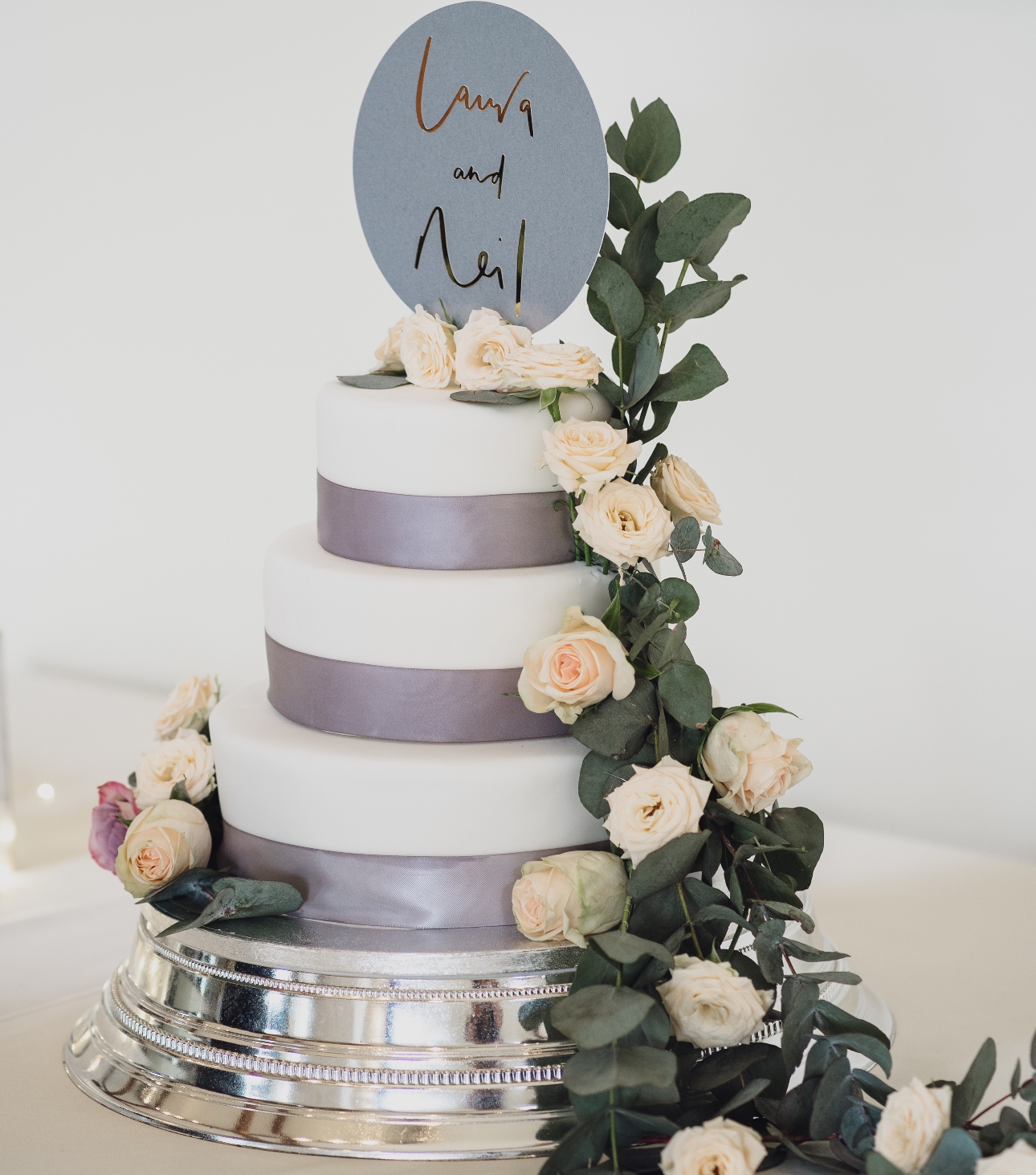 White three-tier cake with flowers and a personalised disc topper