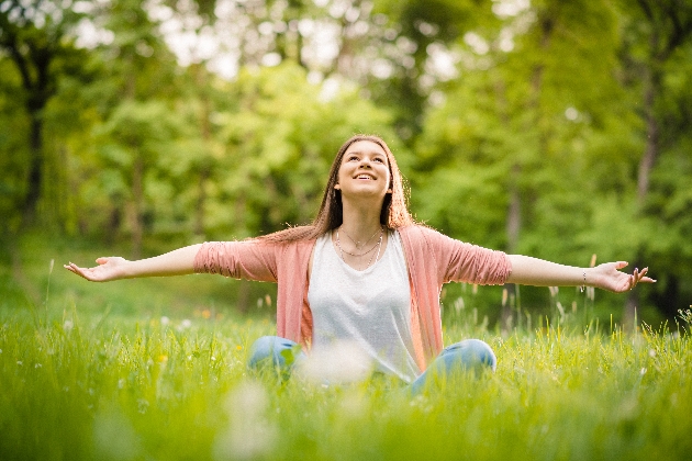 Woman sitting cross legged in the grass with her arms outstretched