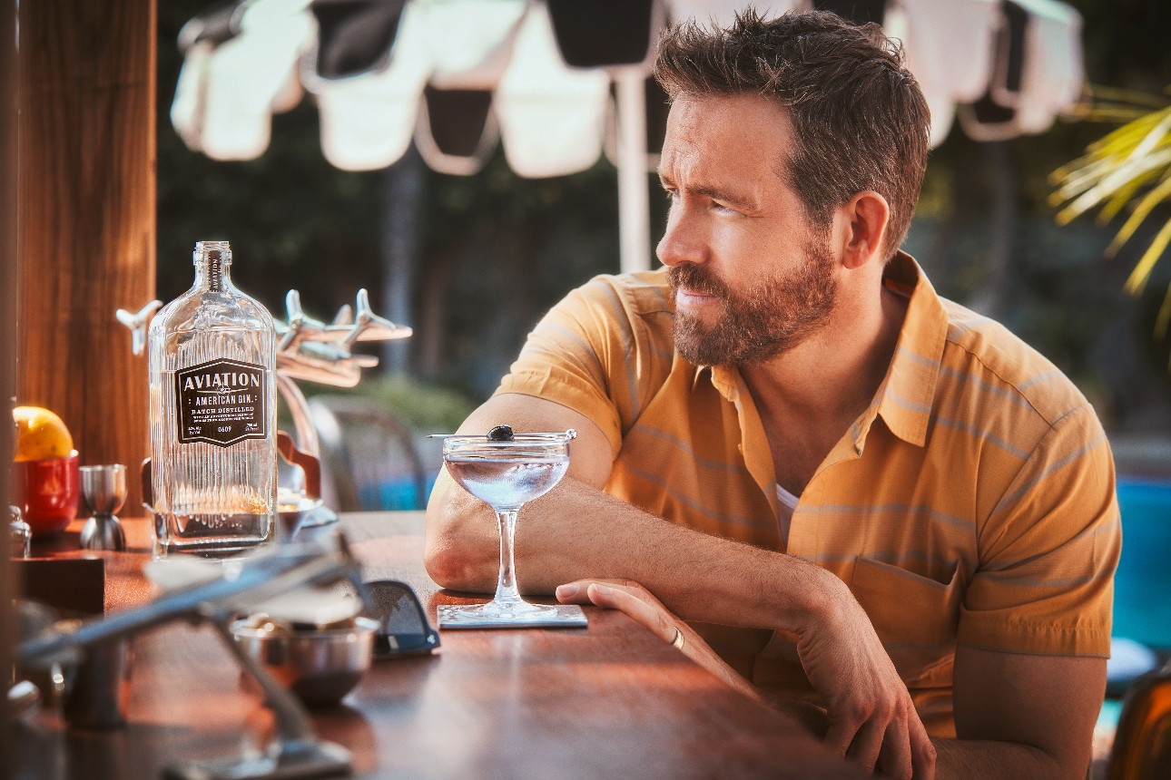 Ryan Reynolds leaning on a pool bar with a cocktail