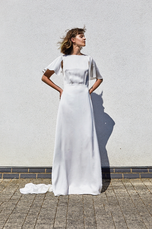 Model wears grey Sabina Motasem dress and stands in front of a grey wall