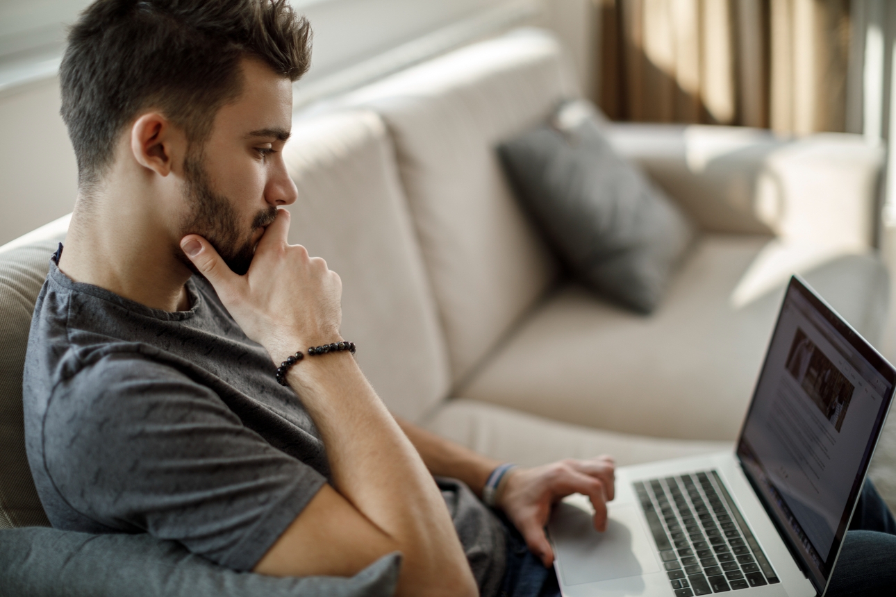 man on sofa looking confused at laptop