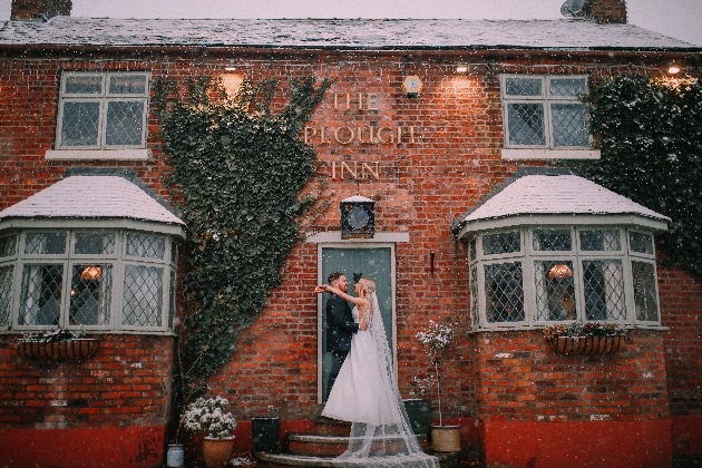 Bride and groom embracing underneath The Plough Inn sign
