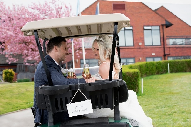 Bride and groom smiling at each other with a glass of wine while sitting in a golf cart