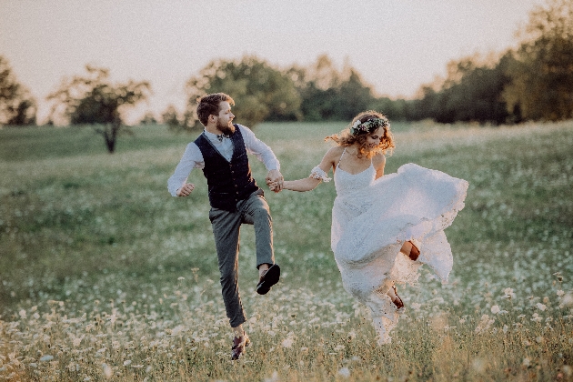 bride and groom dancing through a field of daisies as the sun sets