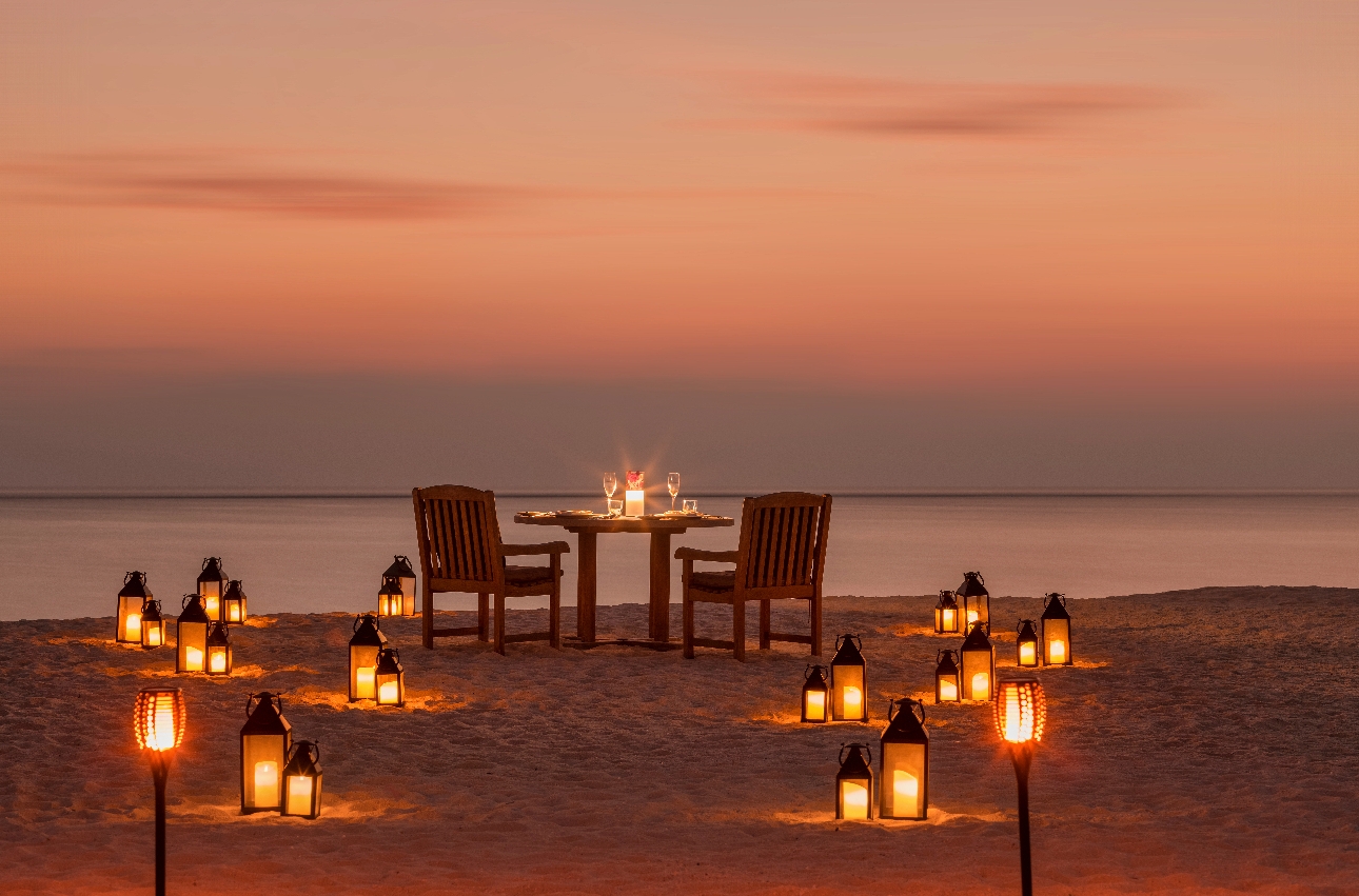 dinner table on beach with candles and lanterns on the ground at sunset