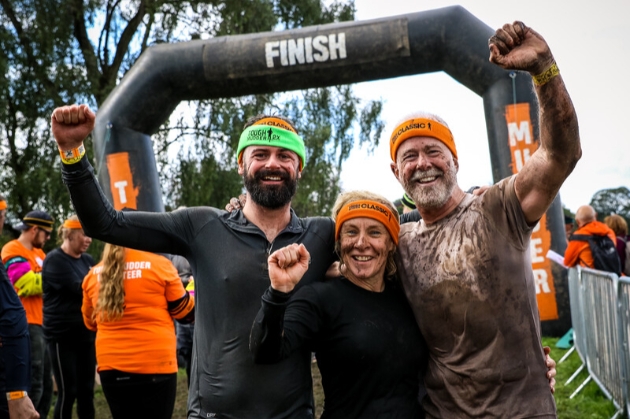 Three people cheering their success at finish line of Tough Mudder event