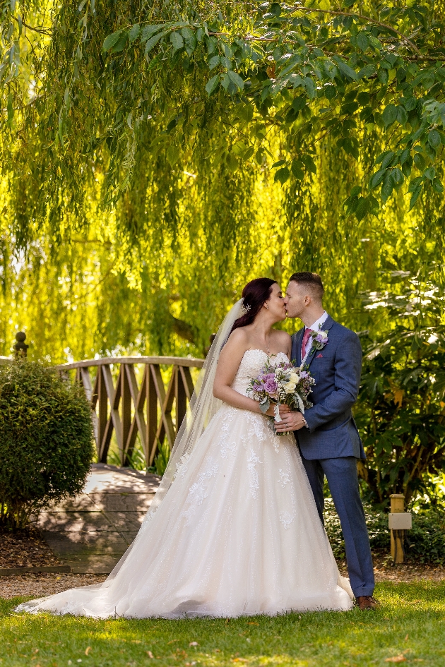 Bride and groom kiss in the grounds of grosvenor pulford chester bridge in background
