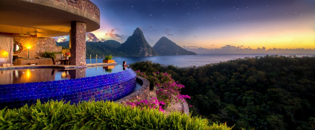 A women in a swimming pool looking out at the sea and St Lucia mountains as the sun sets