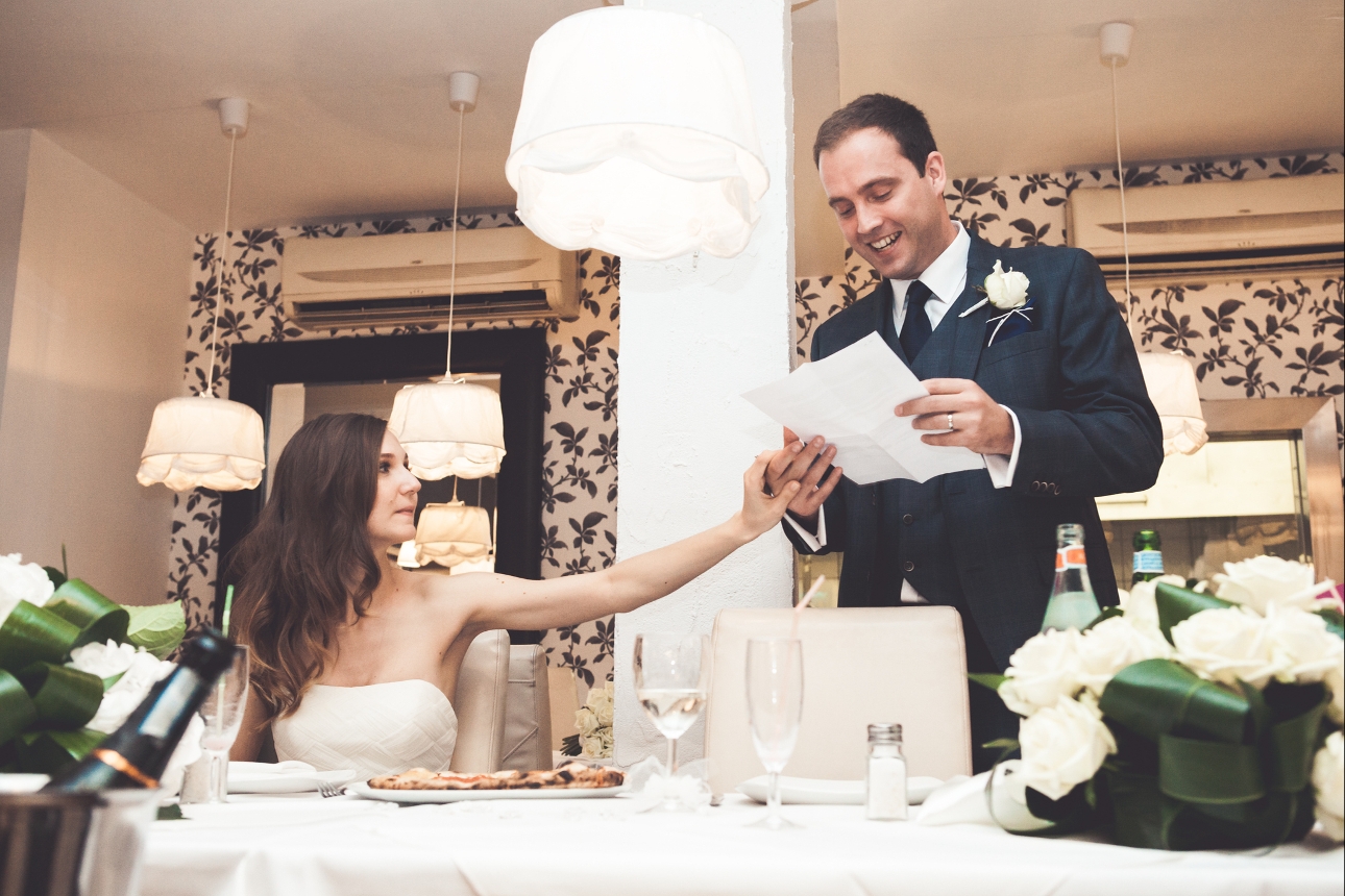 bride touches groom's hand whilst he gives his speech