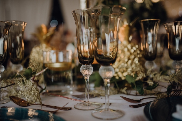 Wedding breakfast table set up with gold and green theme and brown tinted glasses