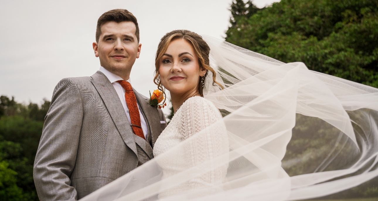 bride and groom with burnt orange theme, bride's veil blowing in the wind