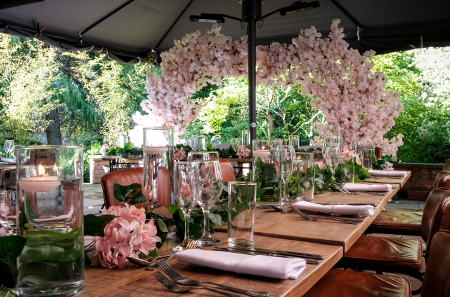 The Bridge Prestbury set up for an al fresco wedding reception pink blossom arch in the background pink floral centrepices
