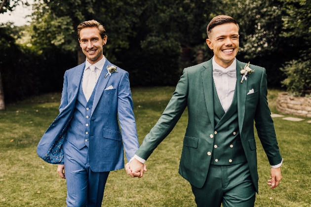 two wedding grooms holding hands wearing King & Allen suits