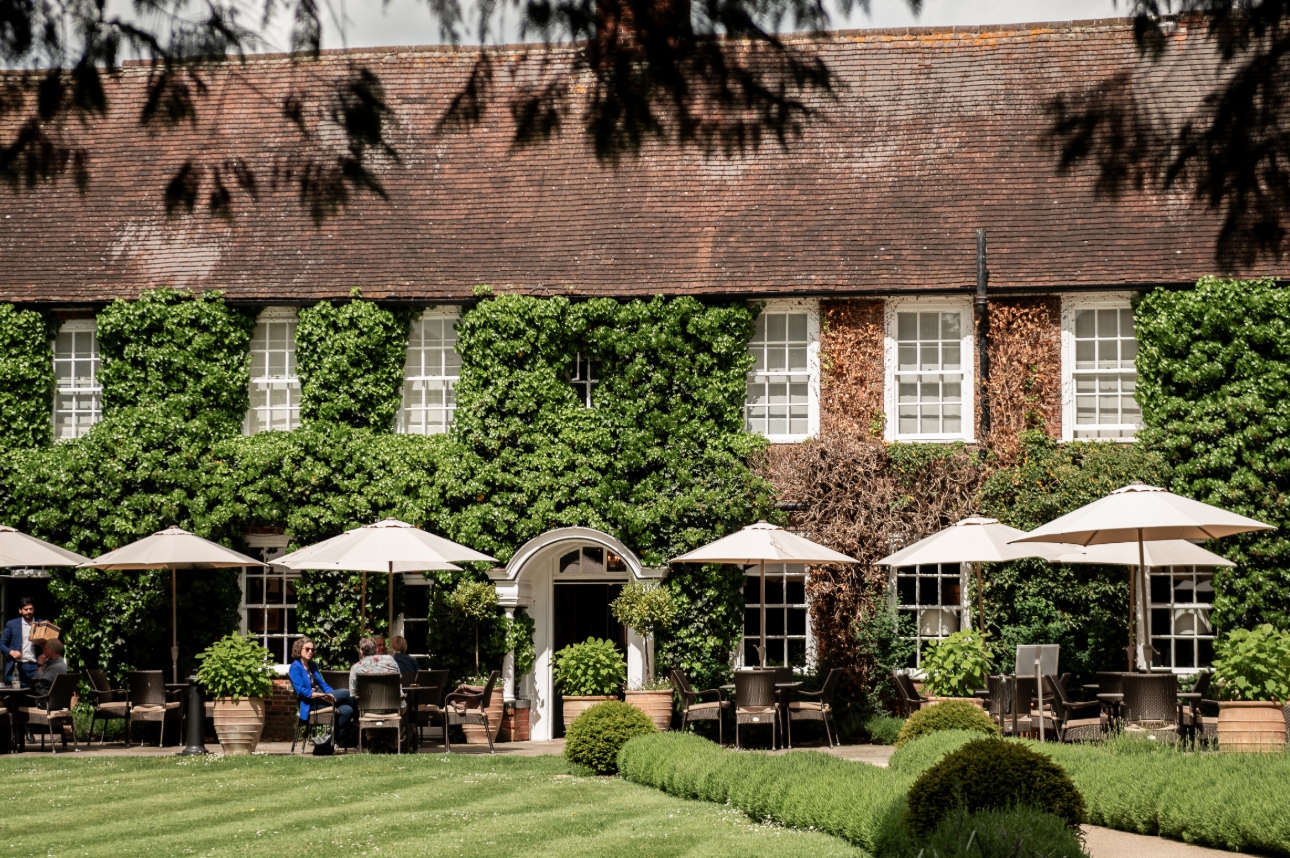old English home with green vines all the way up it and people sat outside