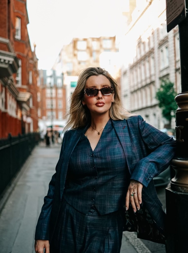 woman wearing navy King & Allen suit and sunglasses leading against a lamppost