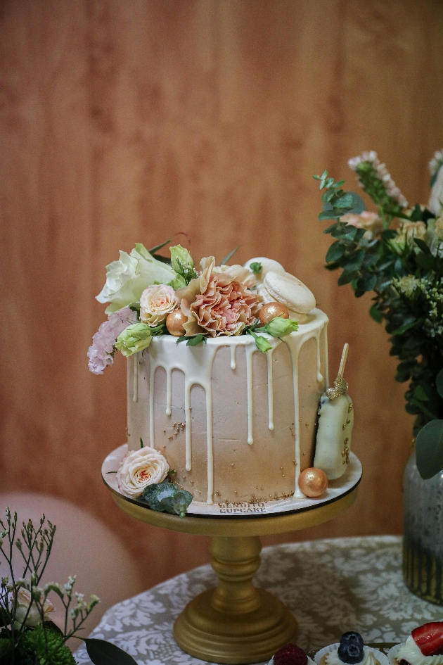 peach and green ombre drip cake topped with flowers and macarons.
