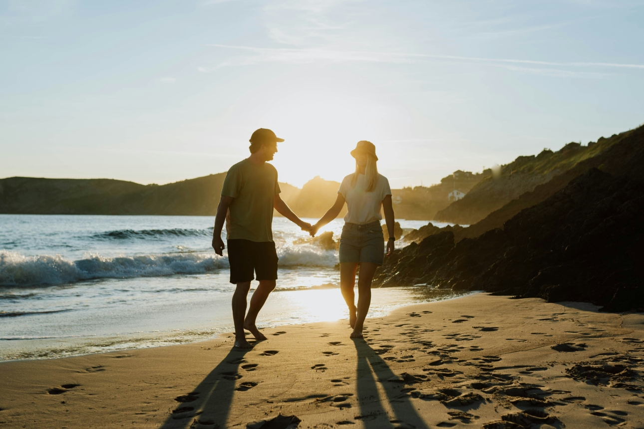 man and woman walking on the beach at sunset